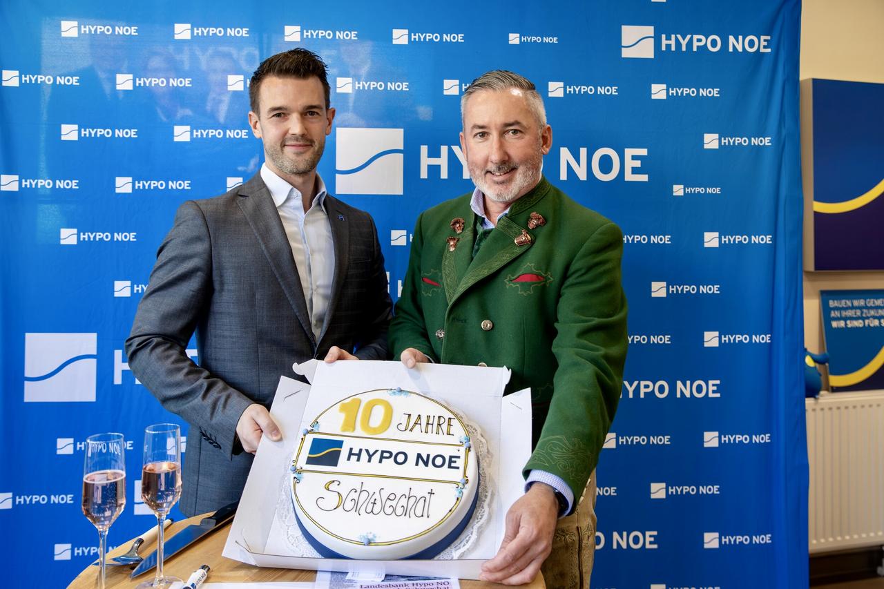 2 Männern und 2 Frauen steht vor einer blauen Wand mit Aufschrift "HYPO NOE" und halten eine Torte in die Kamera.