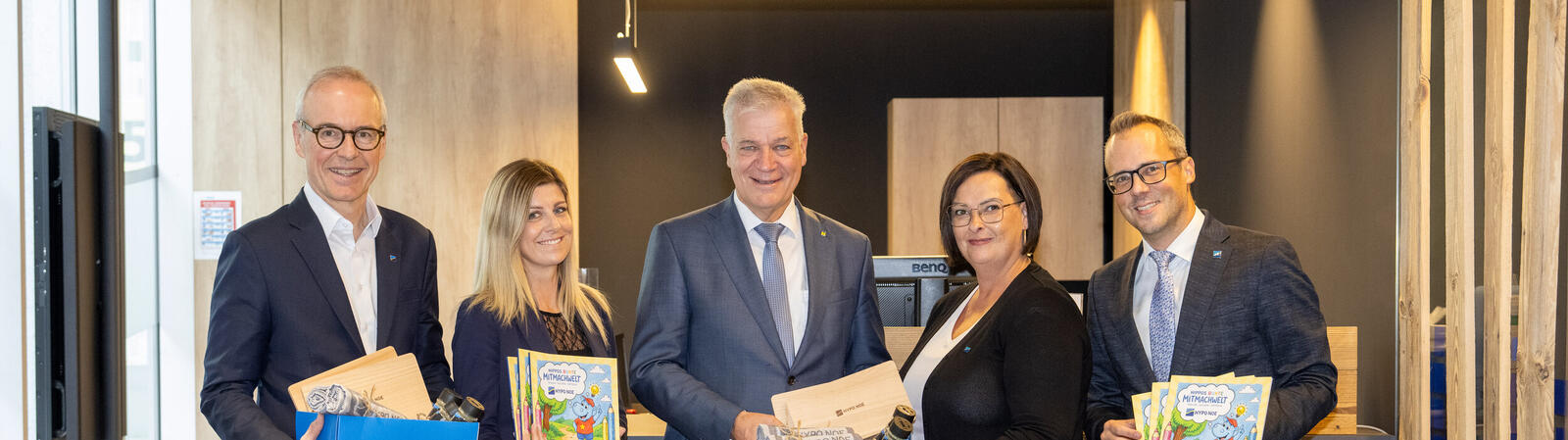 Zwei Frauen und drei Männer halten Geschenkboxen und Malbücher in der Hand.