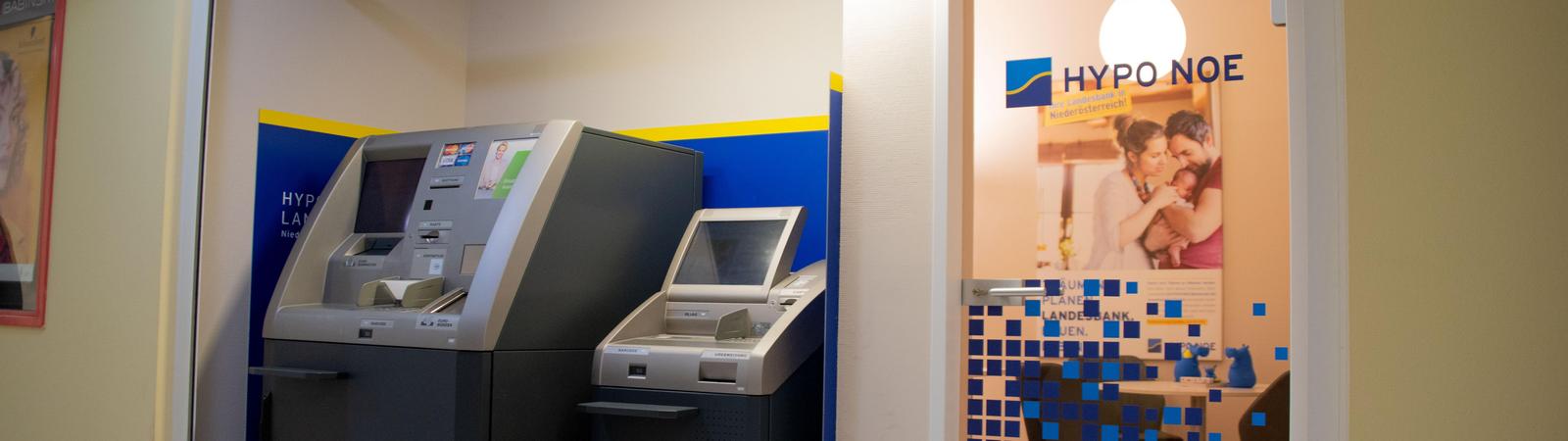 Innenraum mit Bankomat und Kontoauszugsdrucker, rechts ist eine Glastür mit HYPO NOE Logo.