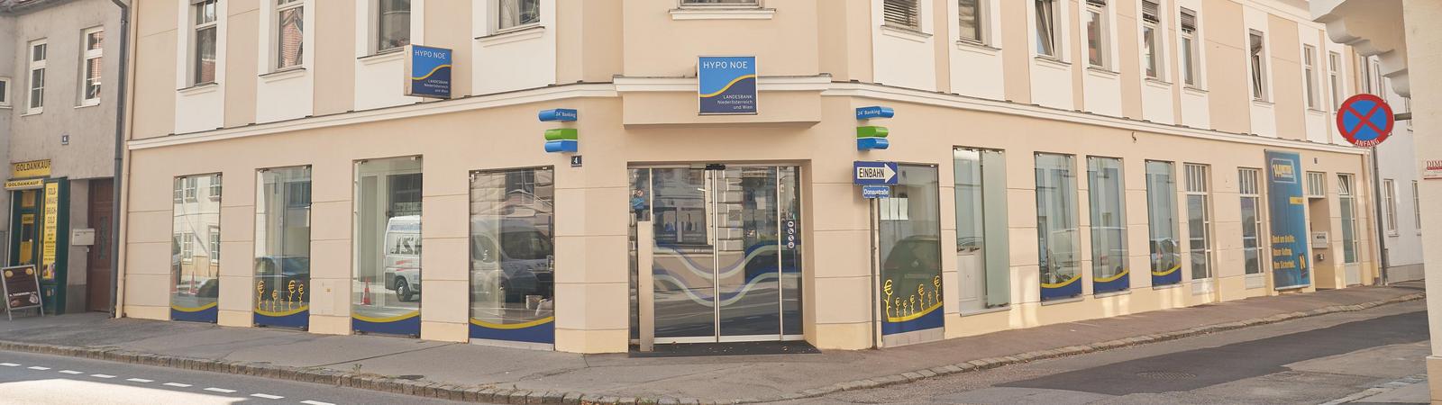 Außenansicht eines zweistöckigen rosafarbenen Gebäudes mit HYPO NOE Logo.