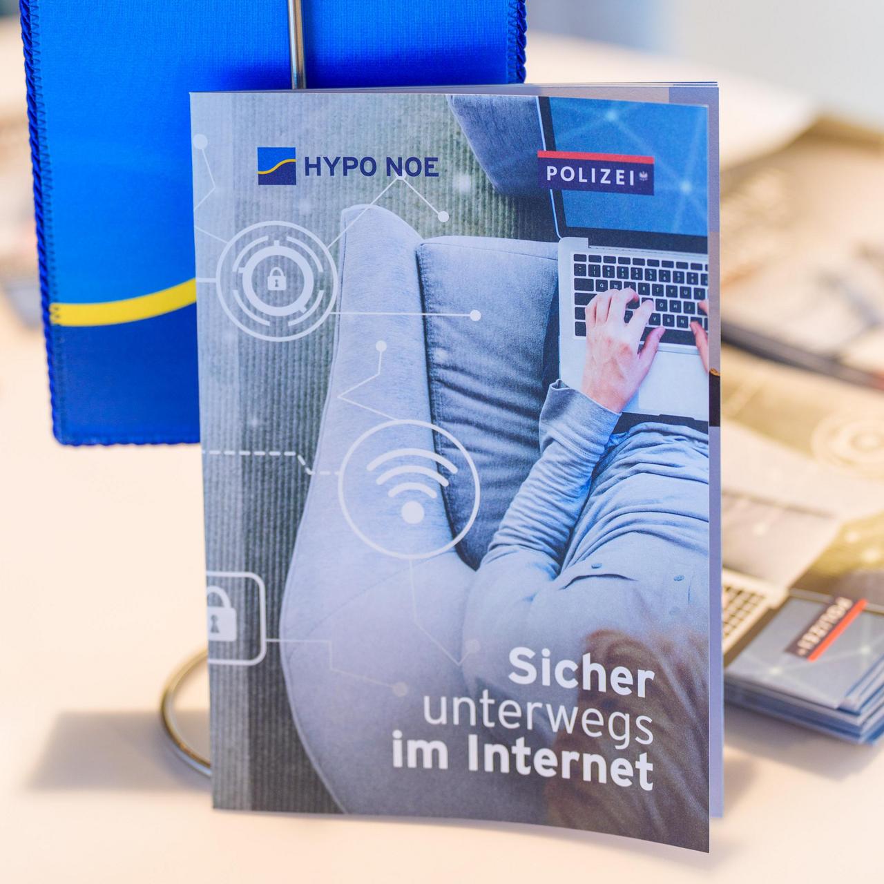 Eine Broschüre steht auf einem Tisch, dahinter sieht man ein Fähnchen mit dem Firmenlogo.