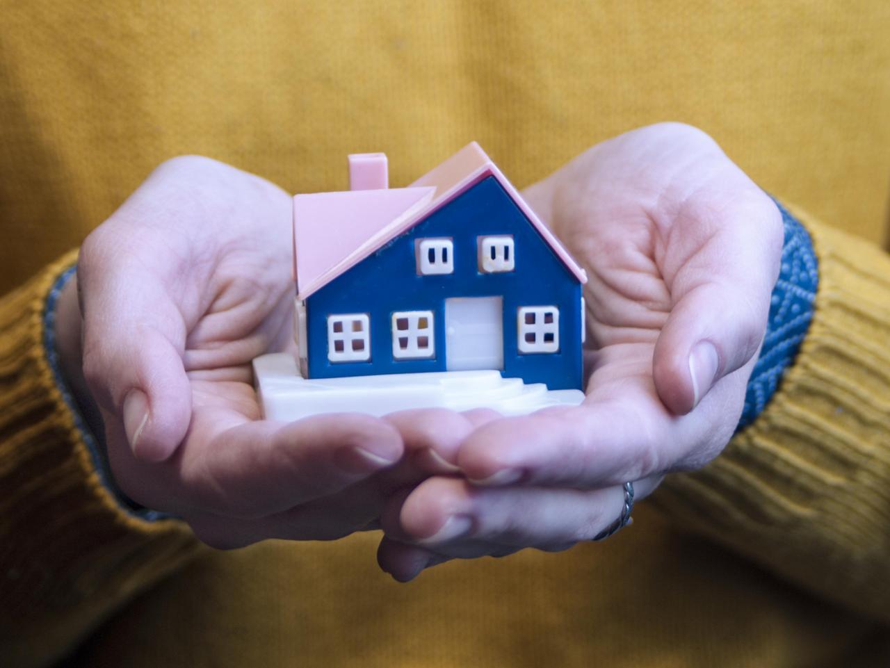 Junge Frau hält die Miniatur eines Hauses in der Hand