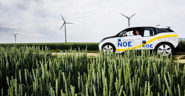Ein Elektrofahrzeug aus dem Fuhrpark der HYPO NOE fährt durch grüne Wiesen - im Hintergrund Windräder